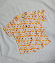 Charger l'image dans la galerie, Children's shirt with half sleeves and a round neckline, featuring a flamingo print in orange and yellow on a white background, laid flat on a grey surface.